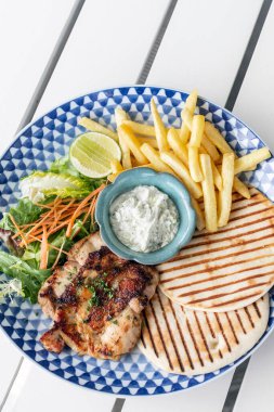 Yunan usulü ızgara tavuk göğsü. Patates kızartması ve salata. Açık havada, Yunan restoranının beyaz masasında.