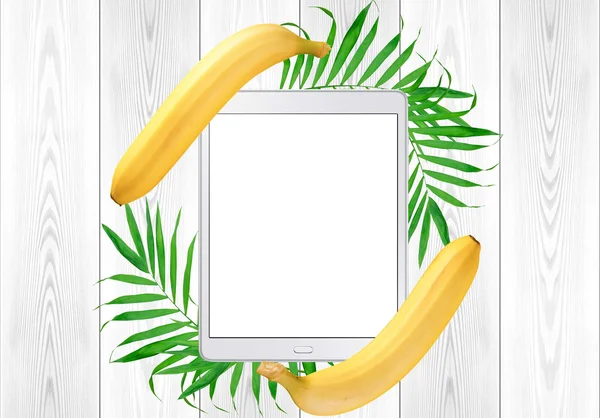 Tablet pc in green fern leaves and banana frame on white wood ta