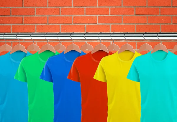 Lots of T-shirts on hangers over orange brick wall