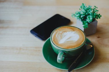 Ahşap arka planda latte sanatıyla birlikte bir fincan kahve. Güzel köpük, yeşil seramik kaplar.