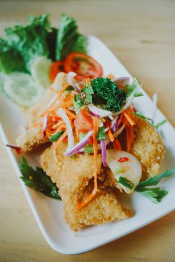 Masaya konmuş baharatlı yağda kızartılmış yayın balığı salatası.