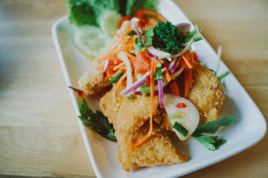 Masaya konmuş baharatlı yağda kızartılmış yayın balığı salatası.