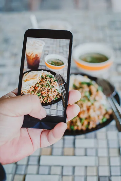 Erkek eli cep telefonuyla Tayland yemeği fotoğrafı çekiyor. Yemek fotoğrafçılığı. Yemek fotoğrafçılığını paylaşın. Popüler yemek fotoğrafı.