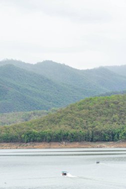 Mavi gölgelikli turistleri taşıyan uzun kuyruklu bir tekne Tayland 'da sakin su ve doğal manzarayla çevrili huzurlu bir göl boyunca süzülüyor. Seyahat ve turizm kavramları için mükemmel bir imaj.
