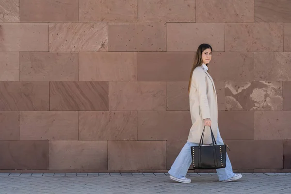 young executive woman walking in sneakers with coat and handbag