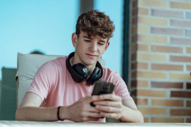 Kahverengi saçlı, kulaklıklı ve akıllı telefonlu genç adam.