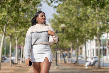 Genç siyahi kadın elinde akıllı telefonuyla yürüyüşe çıkıyor.