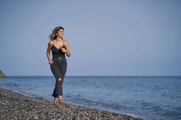 Jeune femme courant le long de la plage vêtue de noir — Photo