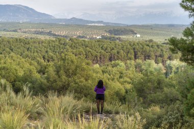 Dağları ve ağaçları olan bir manzarayı izleyen bir kadın.