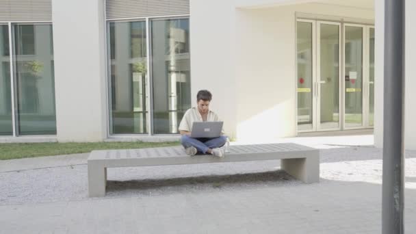 Jeune homme tapant sur son ordinateur portable assis sur un banc — Video