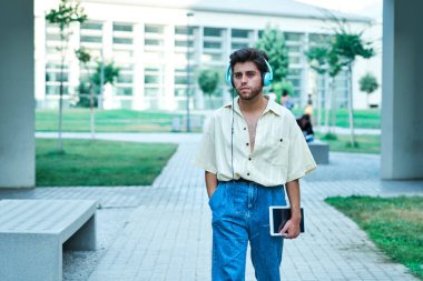 Tabletli öğrenci, üniversite kampüsünde kulaklıkla müzik dinliyor.