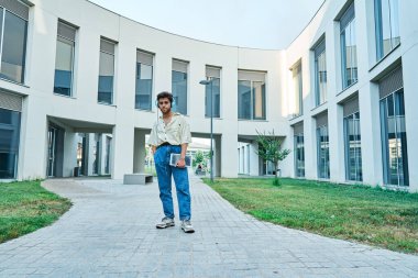 Adam ayakta durup tablet ve kulaklıkla müzik dinliyor.