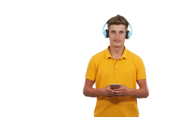 Man in yellow t-shirt listening to music with headphones and his smartphone, while standing against white background. — Stock Photo, Image