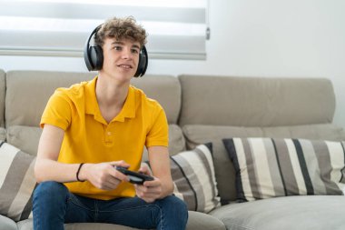 Yakışıklı genç adam oturma odasında kulaklıkla oyun konsolu oynuyor.