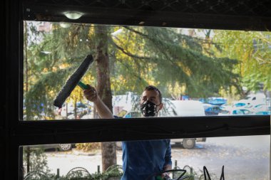 Pencereyi temizliyorum. Yüzünde maske olan genç bir adam pencereleri süngerle temizler ve parlatır.