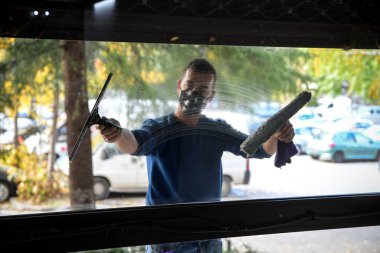 Pencereyi temizliyorum. Yüzünde maske olan genç bir adam pencereleri süngerle temizler ve parlatır.