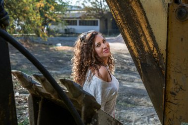 İnşaat makinesinin arkasındaki kız poz veriyor. Güzel güneşli bir gün.