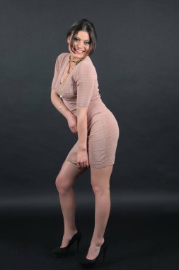 Siyah arka planda örgü örülü açık kahverengi elbise giymiş bir iş kadını portresi. Seksi güzel kadın, güzel yüz, açık kahverengi örgü elbise, koleksiyon stüdyo kataloğu, ofis için esmer aksesuar.