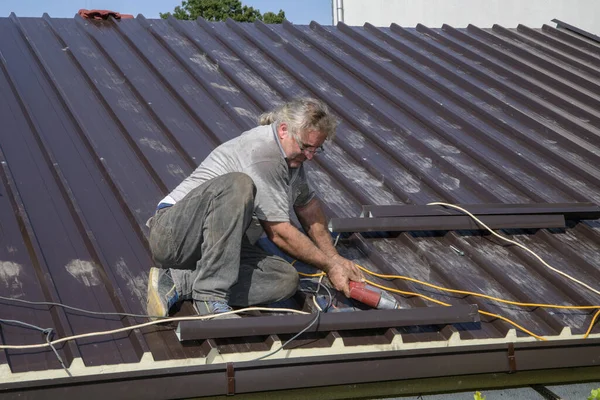 Repairing the roof of the house with screws drive tools. Worker roofer builder working on roof structure