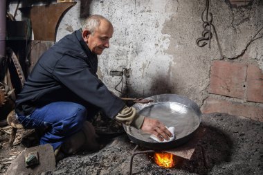 Atölyesindeki yaşlı adam bakır kaseyi tenekeyle kaplıyor. Kalaycı bakır nesneyi alevlerle kaplıyor.