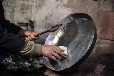 Atölyesindeki yaşlı adam bakır kaseyi tenekeyle kaplıyor. Kalaycı bakır nesneyi alevlerle kaplıyor.