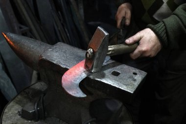 Demirci çekiçle atölyede kızgın demir orağı üzerinde çalışıyor.