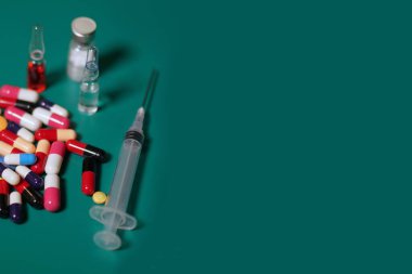 İlaç kapsülleri açık bir reçete şişesinde. İlaç, kapsül, tablet, iğne, şırınga ve iğne. Yeşil arka planda çeşitli uyuşturucuların yakın plan görüntüleri
