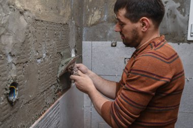 Profesyonel inşaatçı duvara seramik fayanslar yerleştirmeden önce yapıştırıcı sürüyor.