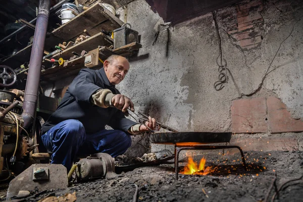Elderly man in his workshop plates the copper bowl with tin. Tinsmith covering the copper object with tin over fire