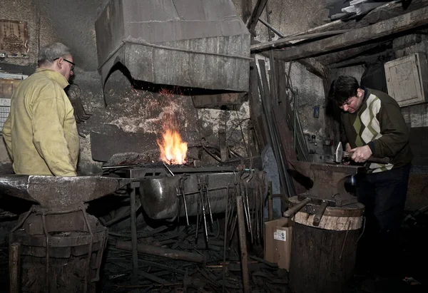 Blacksmiths with hammer working on a heated iron in workshop