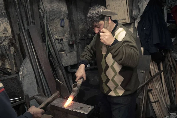 Blacksmiths with hammer working on a heated iron in workshop