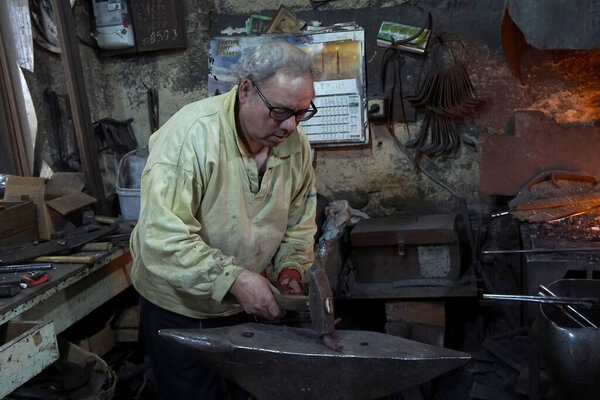 Blacksmith with hammer working on a heated iron rod in workshop 