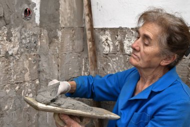 Ev inşaatının duvarına beton yapıştıran kadın işçi.