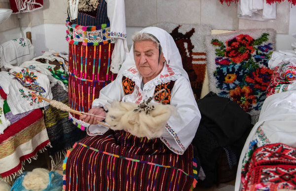 An old woman weaver spun wool on her hand. An old extinct craft