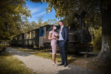 Sağlık maskeli düğün çiftleri parkta poz veriyor. Coronavirüs salgını sırasında maskeli yeni evliler.