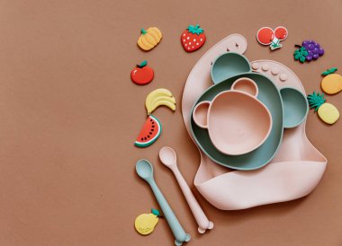 Kahverengi arka planda bebek bulaşık takımı, çocuk aksesuarlarıyla düz kompozisyon, bebek için ilk yemek, ilk beslenme konsepti