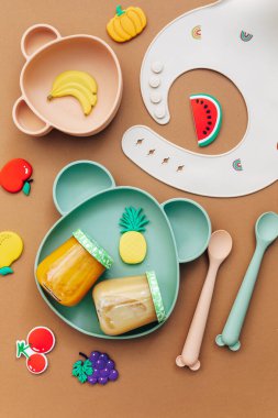 Işık arka planında parlak silikon bulaşık takımı. Bebeğe hizmet etmek, ilk beslenme konsepti. Düz konum, boşluk kopyala, üst görünüm