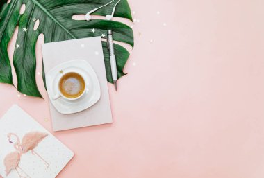 Üst düzey kadın ofis masası, kahve fincanı olan çalışma alanı, pembe arka planda canavar yaprağı.. 