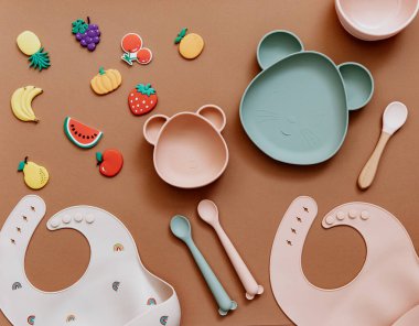 Kahverengi arka planda bebek bulaşık takımı, çocuk aksesuarlarıyla düz kompozisyon, bebek için ilk yemek, ilk beslenme konsepti