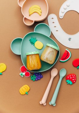 Işık arka planında parlak silikon bulaşık takımı. Bebeğe hizmet etmek, ilk beslenme konsepti. Düz konum, boşluk kopyala, üst görünüm