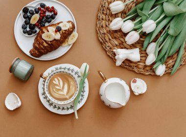 Paskalya, bahar, 8 Mart, Anneler Günü, natürmort. Kahverengi zemin üzerinde beyaz laleler ve kahve fincanı, üst görünüm, düz döşeme, kopyalama alanı 