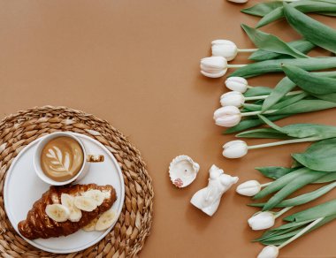 Anneler Günü, 8 Mart, günaydın. Beyaz laleler, kahve fincanı ve kruvasan kahverengi arka planda, üst manzara, düz yatış 