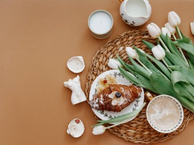 Paskalya, bahar, 8 Mart, Anneler Günü, natürmort. Beyaz laleler, kruvasan ve kahve fincanı kahverengi arka planda, kahvaltı sahnesi. 