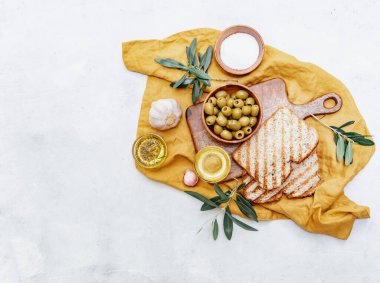 Zeytinyağlı yeşil zeytinler taze pişmiş ciabatta ekmeği, tuz ve beyaz zemin üzerinde taze zeytin dalları. Düz uzanış, boşluk