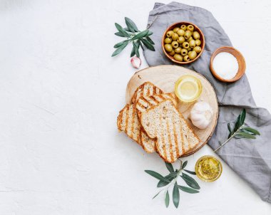 Zeytinyağlı yeşil zeytinler taze pişmiş ciabatta ekmeği, tuz ve beyaz zemin üzerinde taze zeytin dalları. Düz uzanış, boşluk