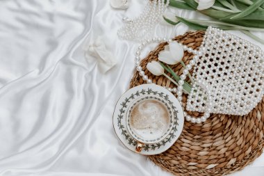 Beyaz laleler, kahve fincanı ve ipek arka planda kadın aksesuarı sabah kahvesi bahar havası. Şatafatlı romantik bir geçmişi var. Kadın sabahı, estetik konsept. Üst manzara, düz uzanma