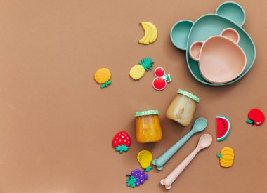 Kahverengi ışık arka planı, üst görünümü, fotokopi alanı, parlak bebek sofra takımı, ilk yemek konsepti için sevimli bebek önlüğü