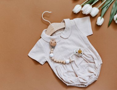 Laleli ve tahta oyuncaklı şirin bir bebek vücudu vardı. Kahverengi arka planda çocuk kıyafetleri ve aksesuarları. Yeni doğan moda.. 