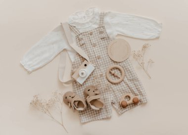 Bebek doğal aksesuar konsepti. Tahta oyuncaklar, kıyafetler ve bej arka planda ayakkabılar. Bohem bebek modası.