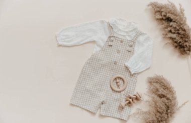 Bebek doğal aksesuar konsepti. Tahta oyuncaklar, kıyafetler ve bej arka planda ayakkabılar. Bohem bebek modası.